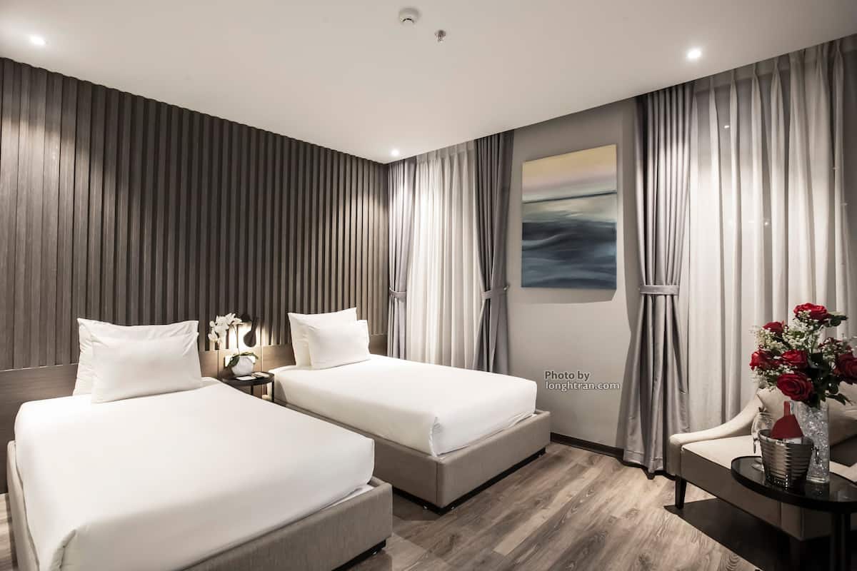 Una habitación de hotel moderna con dos camas, una mesita de noche, un jarrón de flores y un cuadro en la pared.
