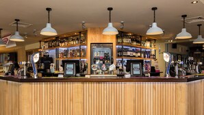 A bar area with wooden paneling, multiple hanging pendant lights, and a variety of bottles and alcohol displayed on shelves.