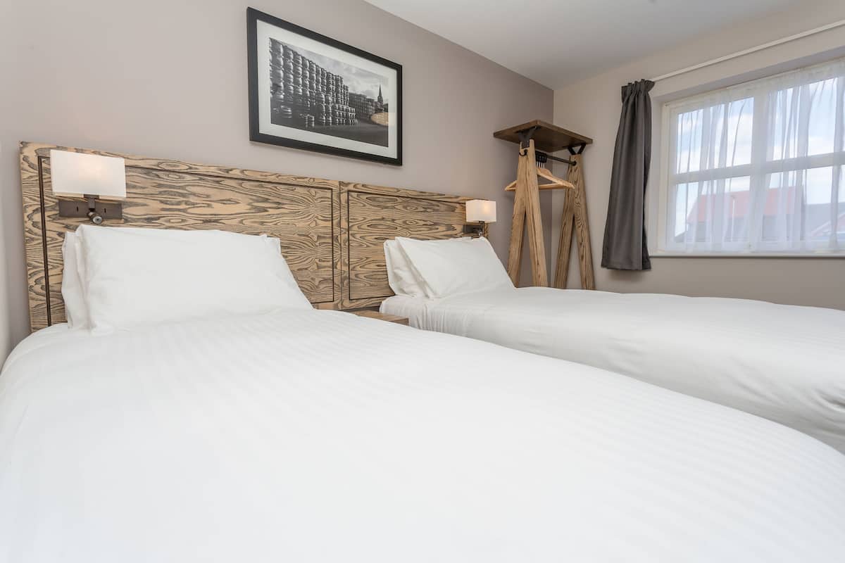 A hotel room with two beds, a framed picture on the wall, and a window with curtains.