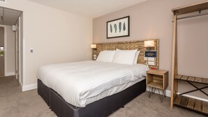 A neatly made bed with a wooden headboard, a small bedside table with a lamp, and a framed artwork on the wall.