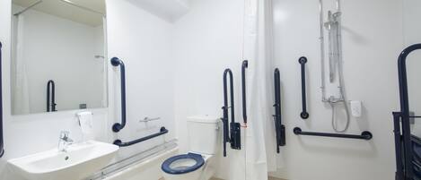 Un baño moderno con un lavamanos blanco, un inodoro con asiento azul, una ducha con cabezal de ducha manual y barras de apoyo.