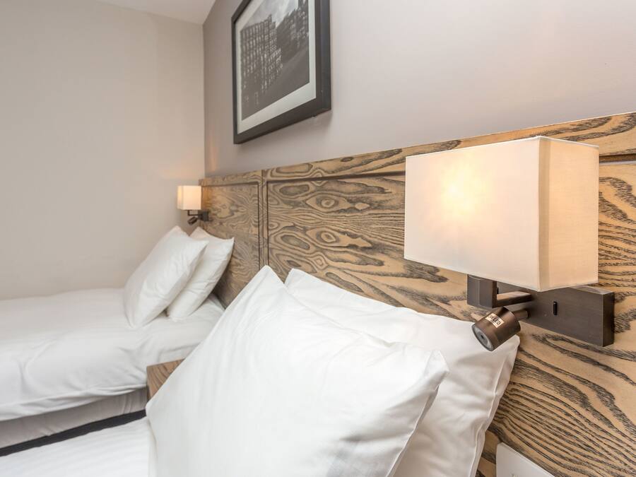 A hotel room with two beds, a wooden headboard, a wall-mounted lamp, and a framed picture above the beds.