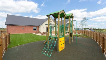 Ein Spielplatz mit einer Kletterkonstruktion und einem Backsteingebäude im Hintergrund.