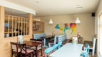 Un restaurant avec des chaises en bois et bleues, une table blanche et une fresque murale colorée représentant des animaux.
