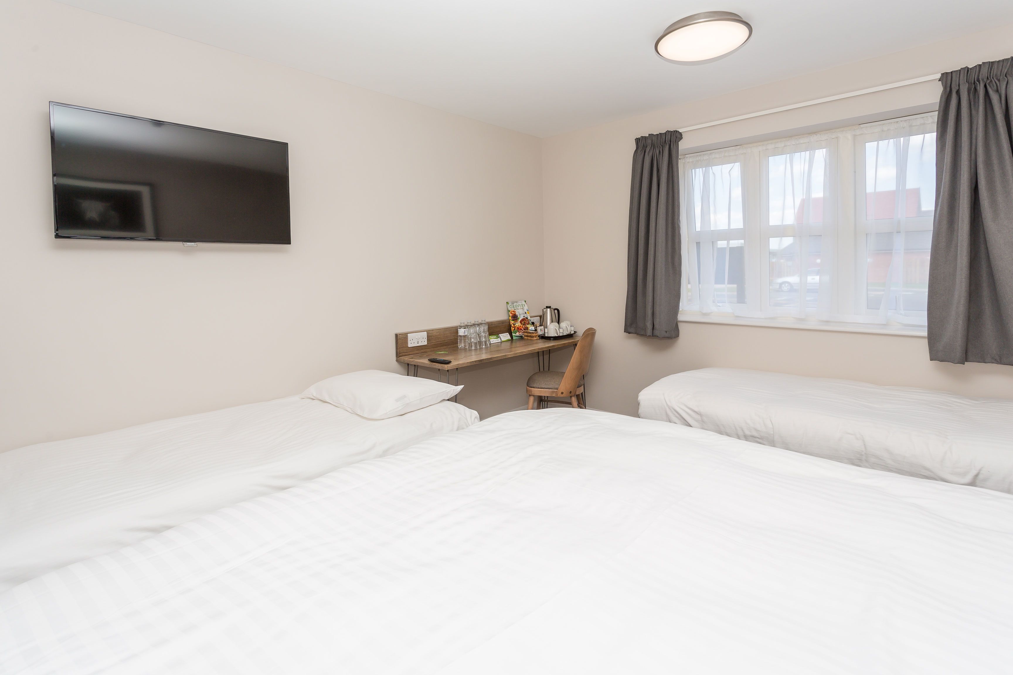 A hotel room with two beds, a desk, a chair, and a TV mounted on the wall.