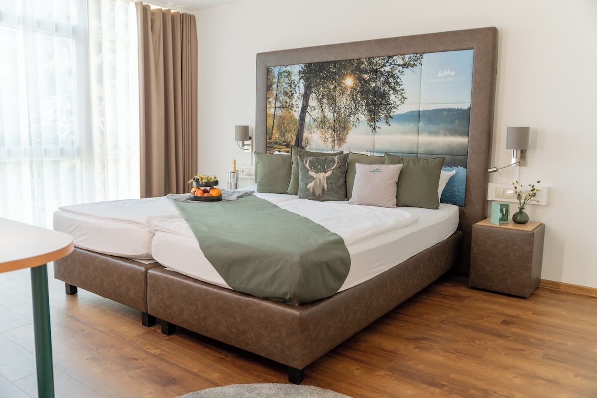 Habitación de hotel moderna con una cama grande, una mesita de noche, una lámpara y vistas al exterior a través del ventanal.
