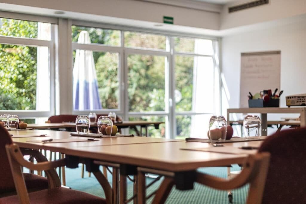 A dining area with tables and chairs, a whiteboard, and a view of greenery outside.