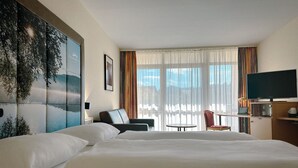 A hotel room with a large bed, a desk with a chair, a television, and a view of the outdoors through the window.