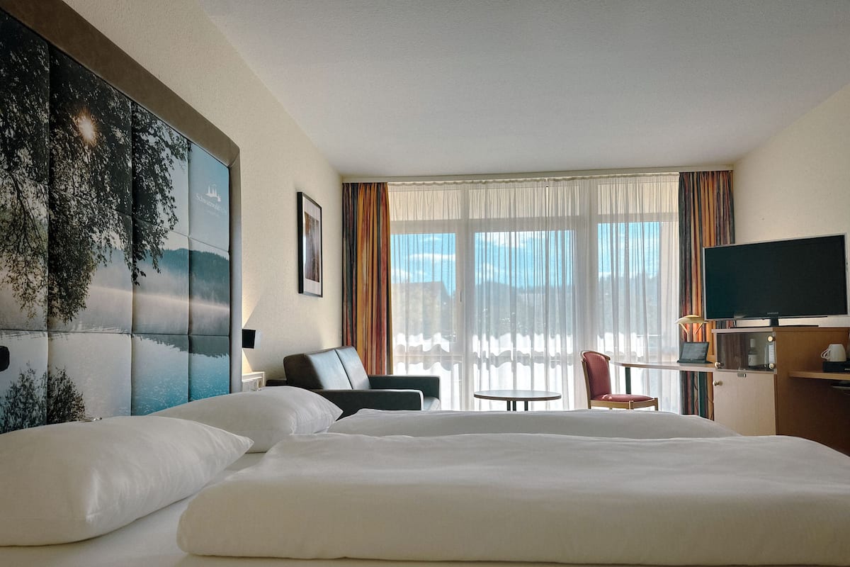 Habitación de hotel con una cama grande, un escritorio con silla, televisión y vistas al exterior a través de la ventana.