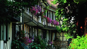 A traditional European-style building with a cobblestone courtyard, multiple balconies with hanging flowers, and a stone wall.