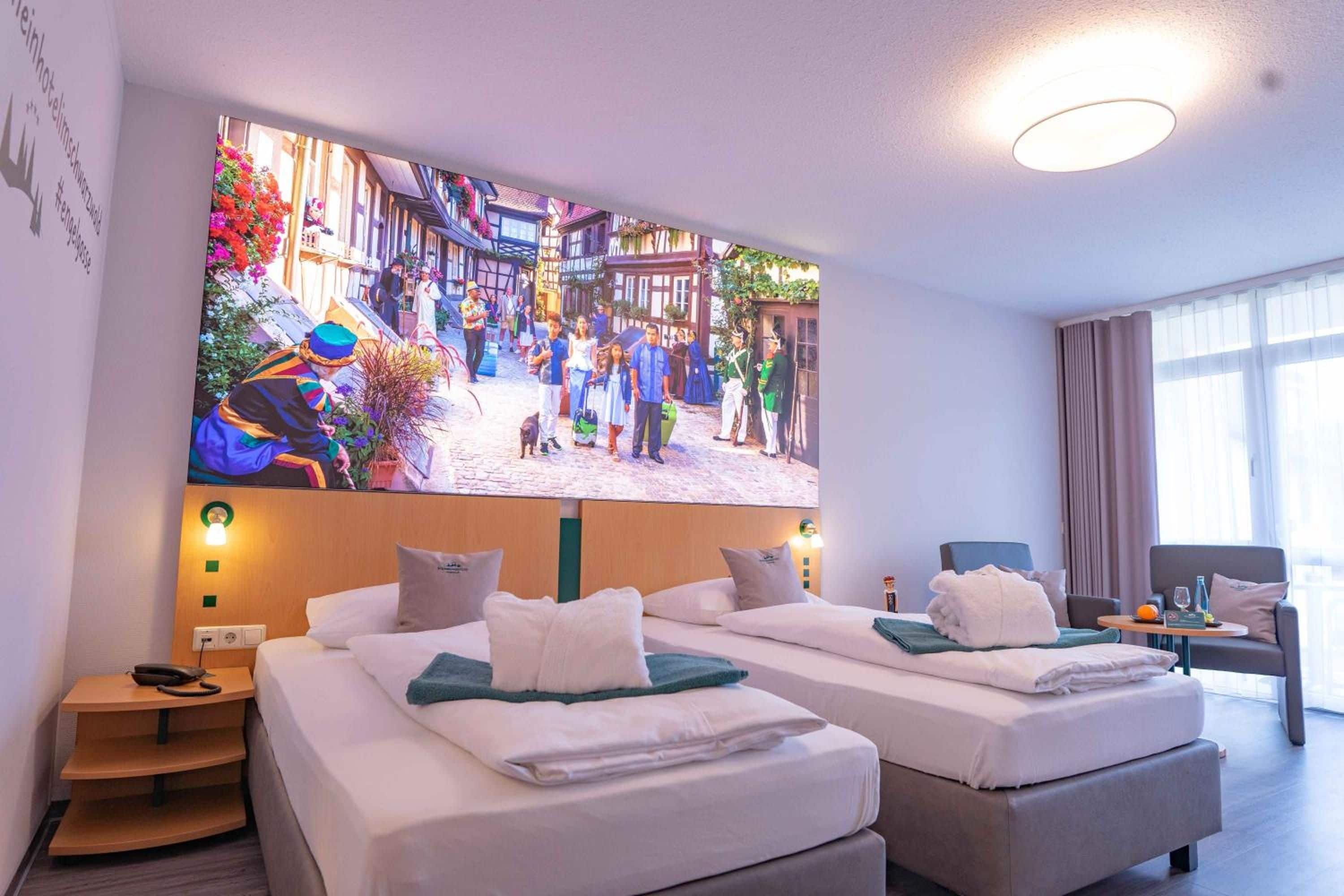 A hotel room with two beds, a large wall mural, a small table, and a chair.