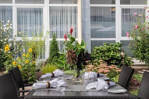 An outdoor dining area with a table set for four, surrounded by lush greenery and flowers. - Schwarzwaldhotel Gengenbach (Gengenbach)