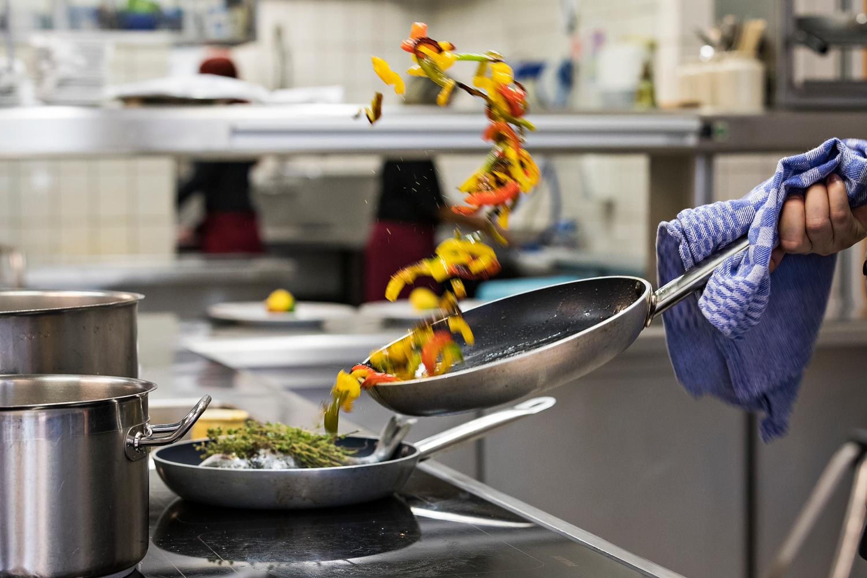 A kitchen with stainless steel cookware, a blue cloth, and a pot on the counter.