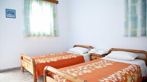 A room with two wooden beds, each with an orange floral bedspread. There is a window with a curtain, and a small framed picture on the wall. - Apartment Alex for 4 (Mykonos)