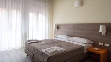 Un letto rifatto con copriletto trapuntato, un comodino con un piatto e una lampada fissata al muro.
