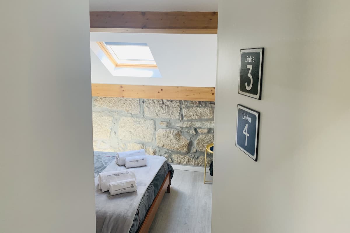 A bedroom with a skylight, a bed with towels, and a stone wall. There are two signs on the wall indicating room numbers 3 and 4.