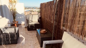 A rooftop terrace with a bamboo wall, a cushioned seating area, and a potted plant.