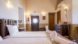 Hotellihuone, jossa on suuri sänky, puinen pääty, kivestä tehty korosteseinä, lipasto ja peili.