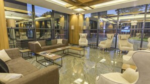 A modern lounge area with sofas, armchairs, and a coffee table. Large windows offer views of the outside. - Shimall Hotel (Gaziantep)