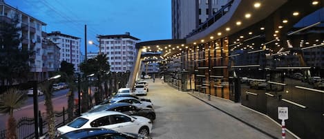 Ein moderner Hotelzugang mit überdachtem Gang, parkenden Autos und umgebenden Gebäuden.