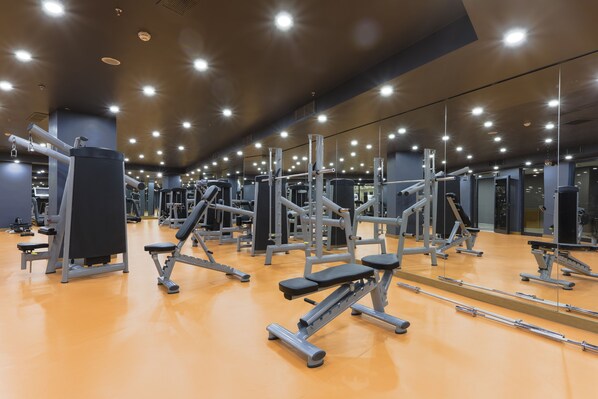 Un gimnasio con diversas máquinas de ejercicio, espejos y un suelo naranja brillante.