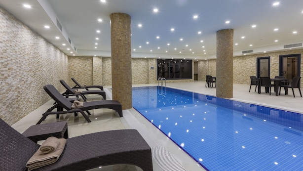 A swimming pool area with lounge chairs and a table, surrounded by stone pillars and recessed lighting. - Shimall Hotel (Gaziantep)