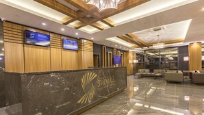 A hotel reception area with a marble counter, wooden paneling, and a modern chandelier. - Shimall Hotel (Gaziantep)