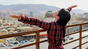 Una persona en un balcón, con vistas a un paisaje urbano y montañas al fondo.