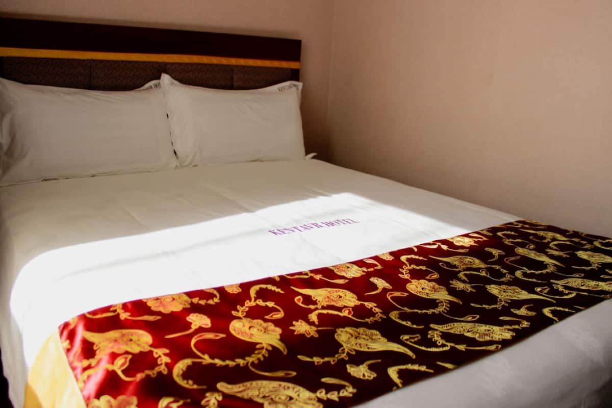 A bed with white linens and a red blanket with gold patterns.