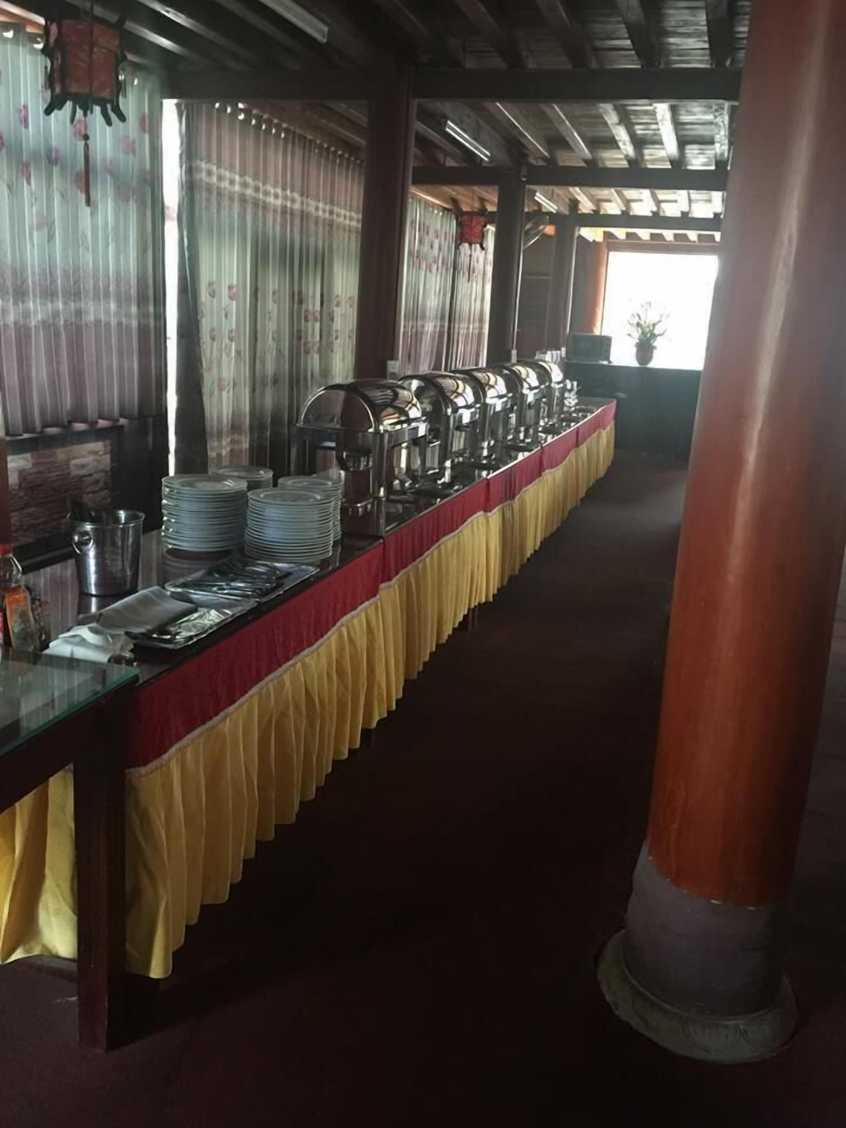 Een lange tafel met een geel-rode tafelkleed, belegd met gestapelde borden en bestek, en voorzien van meerdere koffiezetapparaten.