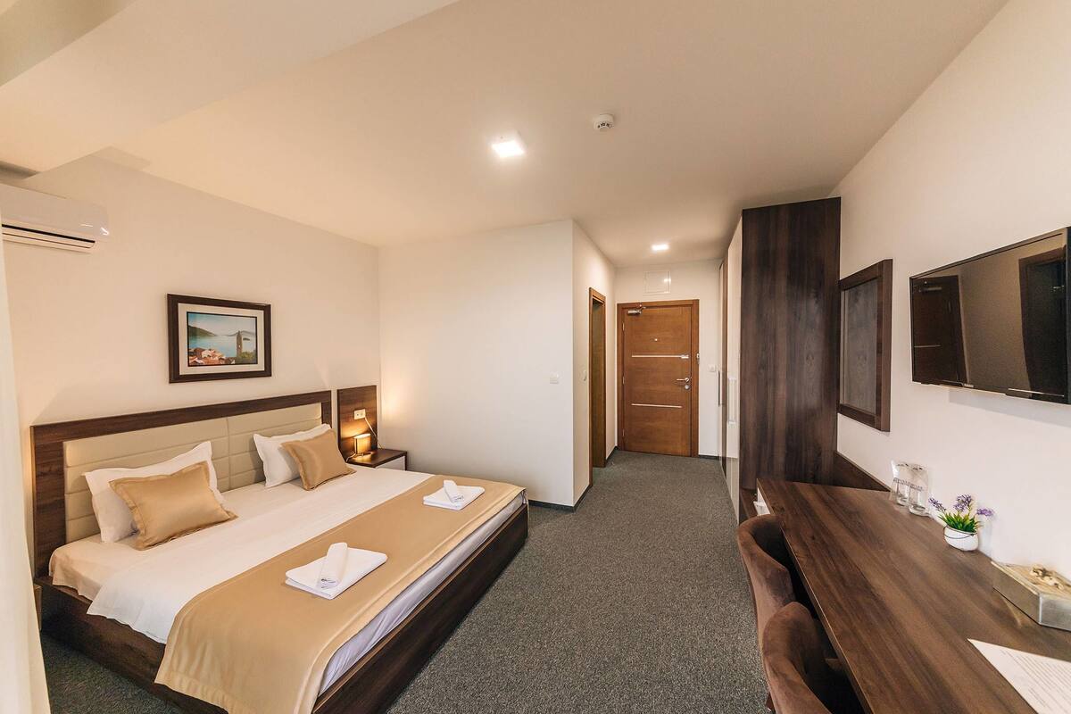 A hotel room with a bed, bedside tables, a desk, and a TV.