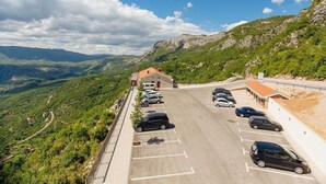 Un estacionamiento con varios coches, un edificio de techo rojo y un paisaje montañoso al fondo.