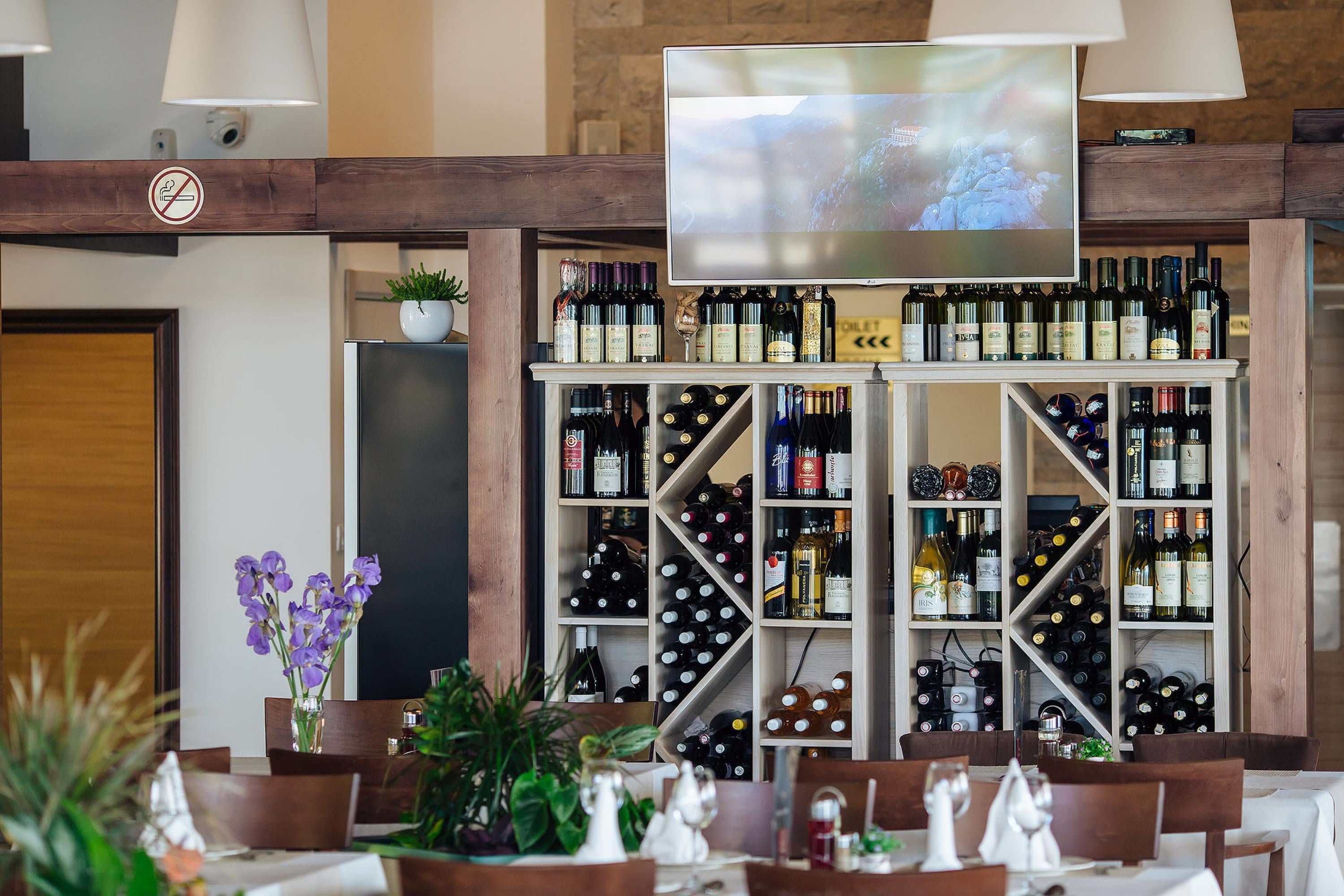 A bar area with a TV screen, wine shelves, and dining tables.