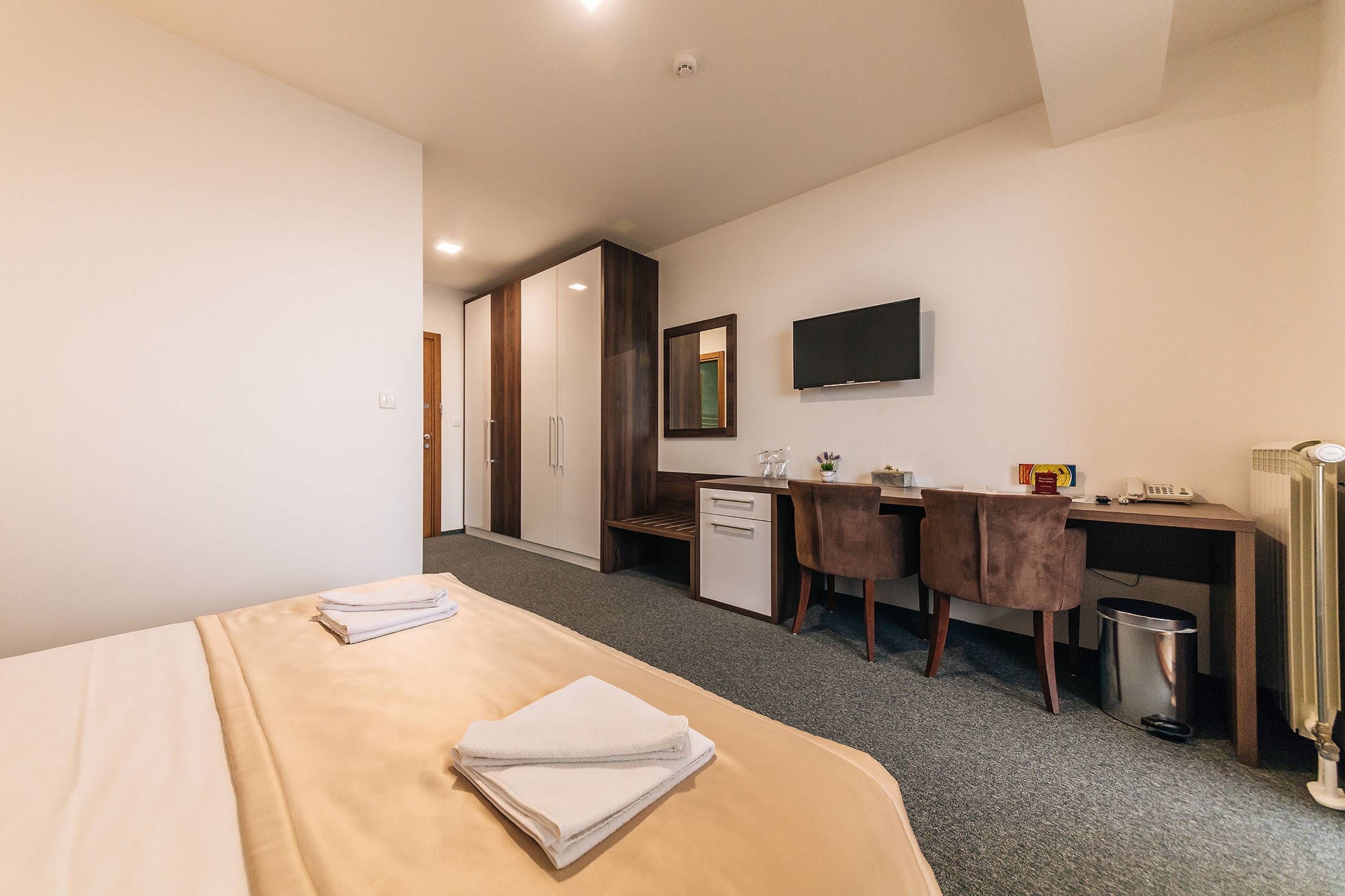 A hotel room with a bed, a desk, a chair, a television, and a radiator.