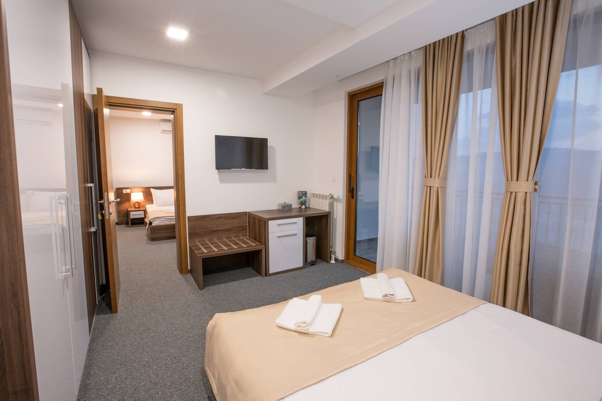 A hotel room with a bed, a desk, a chair, a TV, and a window with curtains.
