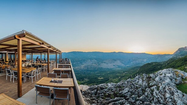 Un restaurante al aire libre con mesas y sillas de madera, con vistas a un paisaje montañoso.