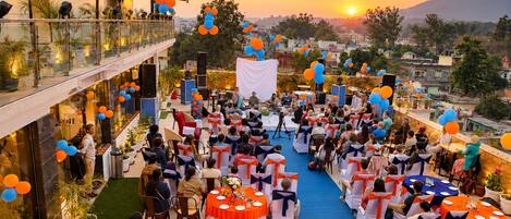 An outdoor event with tables and chairs arranged for guests, a stage for speakers, and a scenic sunset view.