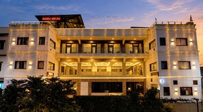 A multi-story hotel with a balcony on the second floor, a sign above the entrance, and a well-lit facade. - Indira Nikunj Rubystone Exotic (Narendranagar)