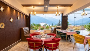A restaurant with a mountain view, featuring red and yellow chairs, a booth seating area, and a table set with plates and cutlery. - Indira Nikunj Rubystone Exotic (Narendranagar)