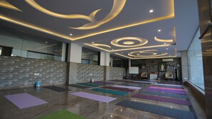 Une pièce spacieuse dotée d’un plafond au design moderne, d’un mur en briques et de plusieurs tapis de yoga disposés sur le sol.