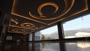 Un hall d’entrée moderne doté d’un sol réfléchissant, de grandes fenêtres offrant une vue sur les montagnes et d’un plafond orné de luminaires circulaires.