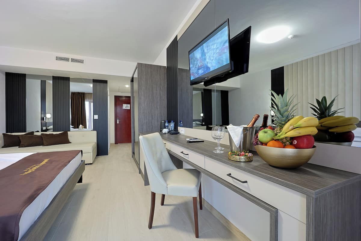 A hotel room with a bed, a desk with a computer, a television, and a fruit bowl.