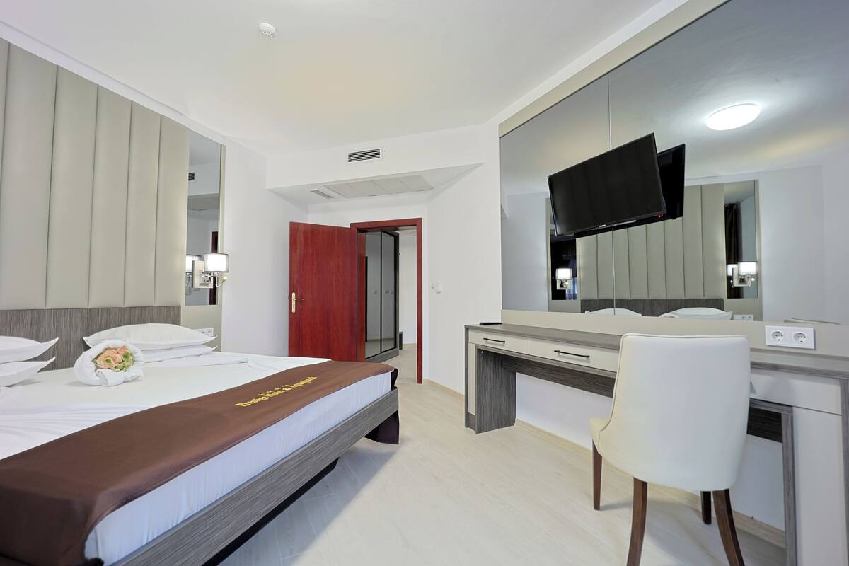 A hotel room with a bed, a desk, a chair, a TV, and a mirror.