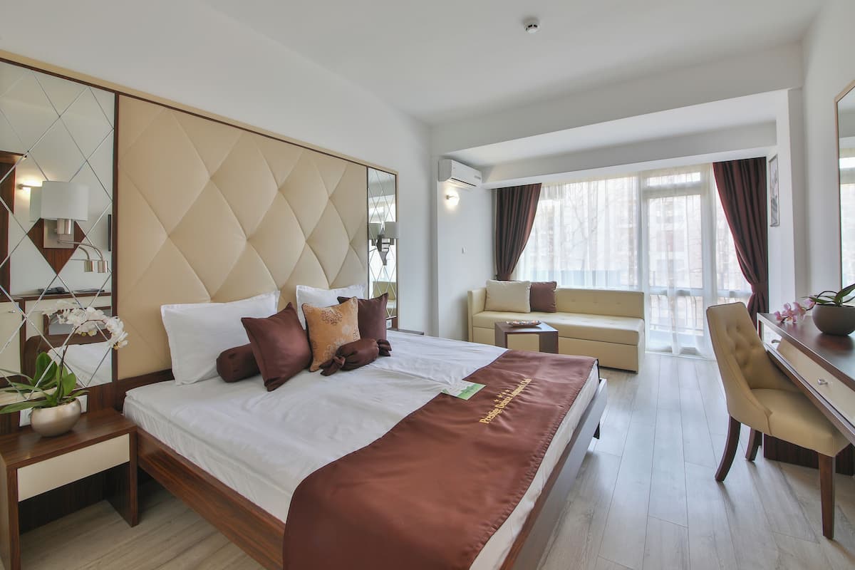 A hotel room with a large bed, a desk, a sofa, and a TV.