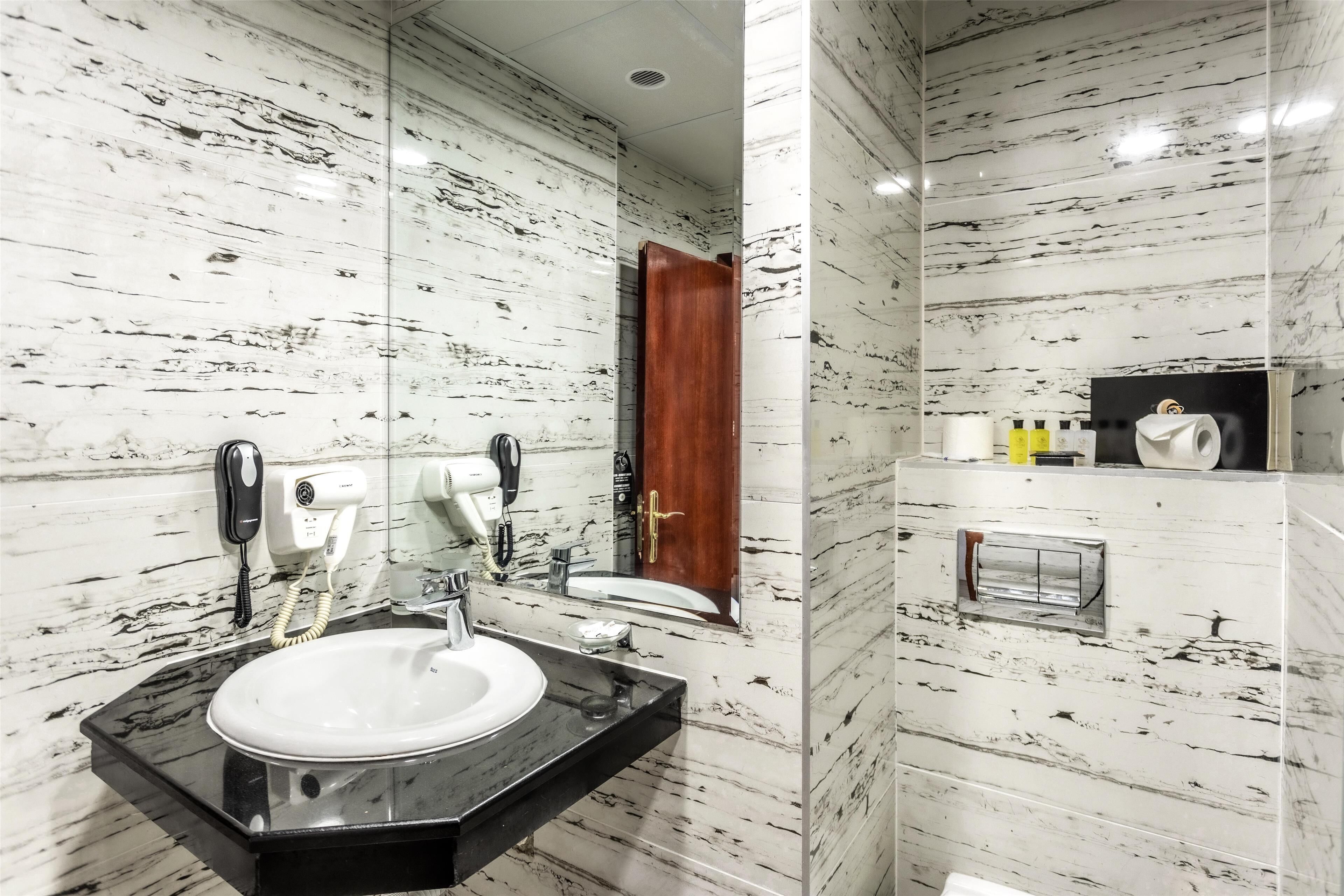 A bathroom with a marble wall, a sink, a mirror, a hairdryer, and a toilet.
