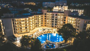 A multi-story hotel with a central courtyard featuring a swimming pool, outdoor seating, and a water slide. - Prestige Hotel and Aquapark (Golden Sands)