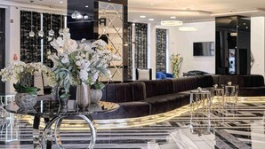 A modern lobby with a marble floor, a round glass table with vases of flowers, a dark leather sofa, and a seating area with small tables and chairs. - Prestige Hotel and Aquapark (Golden Sands)