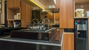 A modern kitchen with a gas stove, stainless steel appliances, wooden cabinets, and a water dispenser. - 3BR with Sofa bed at Gateway Pasteur Apartment (Cimahi)