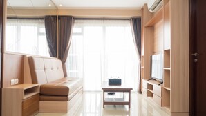A modern living room with a sofa, TV, and wooden furniture. - 3BR with Sofa bed at Gateway Pasteur Apartment (Cimahi)