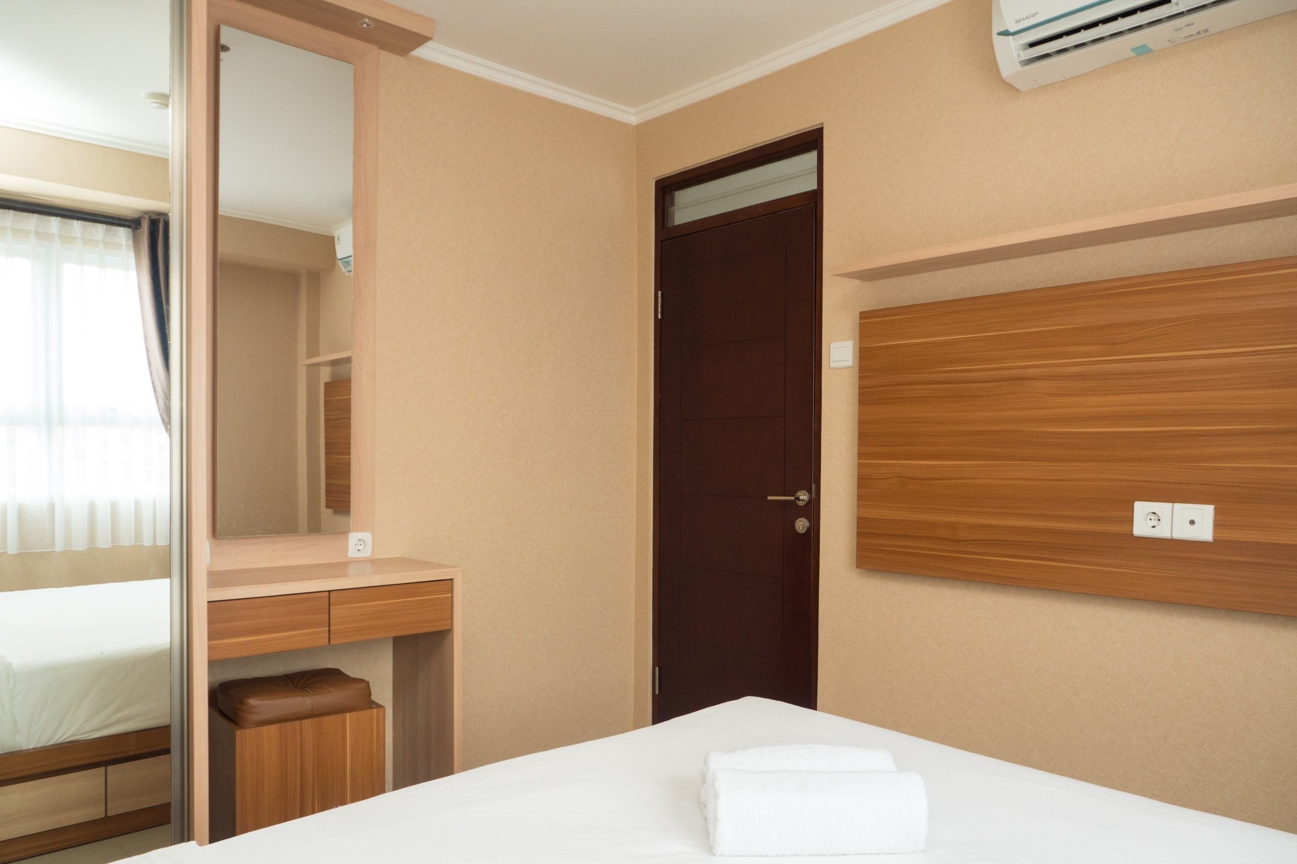 Habitación de hotel con cama, escritorio, espejo, armario y unidad de aire acondicionado.